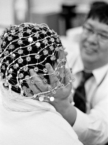 The image shows a researcher fitting an EEG device onto a person's head.