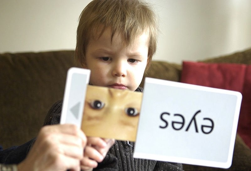 The image shows a child with ASD identifying words from a flash card.