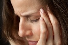The image shows a woman rubbing her head as though she has a migraine.