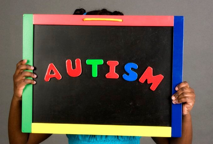 The image shows a child holding a sign with the word autism written on it.