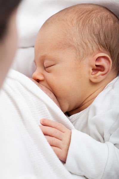 The image shows a baby being breast fed.