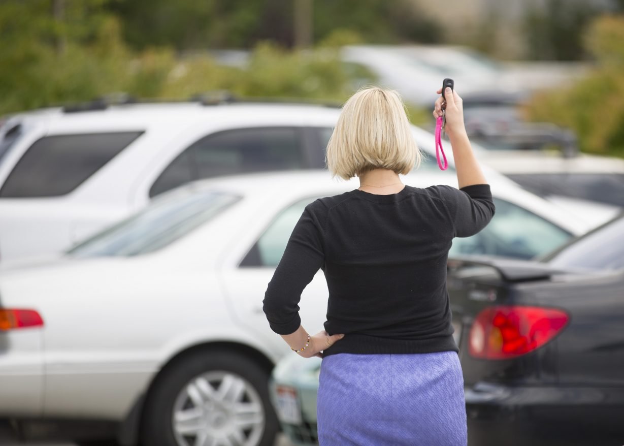 The image shows a woman clicking her keys, looking for her car.