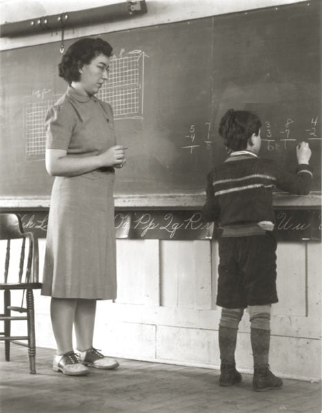 The image shows a teacher in the 1940's with a student.