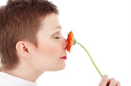 The image shows a woman smelling a flower.