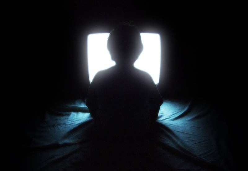 The image shows a child sitting in front of a TV set. The image is dark, as if to imply this image is taken late at night.