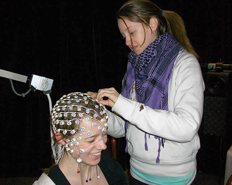 The image shows the researcher putting the EEG headset on a study participant.