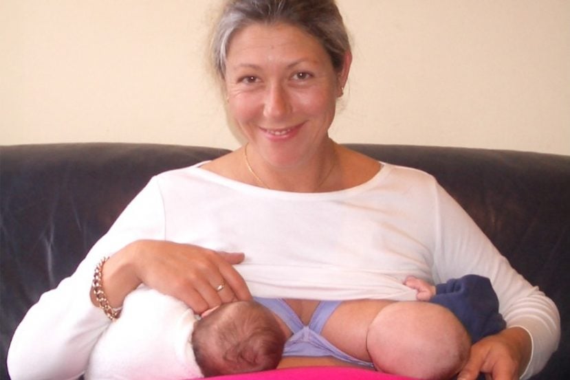 A mom is breastfeeding twins and is smiling.