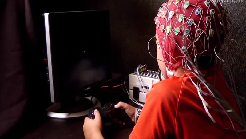 The image shows a still from the video. A little boy is being tested and is wearing an EEG cap.