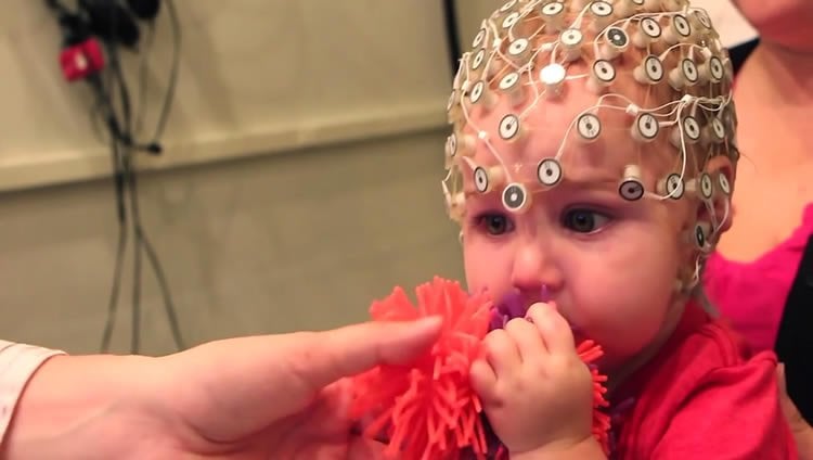 This image shows a baby chewing on a toy with an eeg helm on.