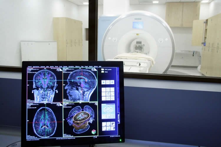This image shows an fMRI machine and brain scan images on a computer screen.
