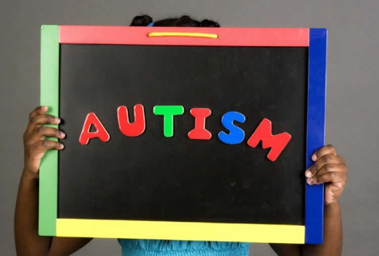 This image shows a child holding up a chalk board with the word Autism written on it.