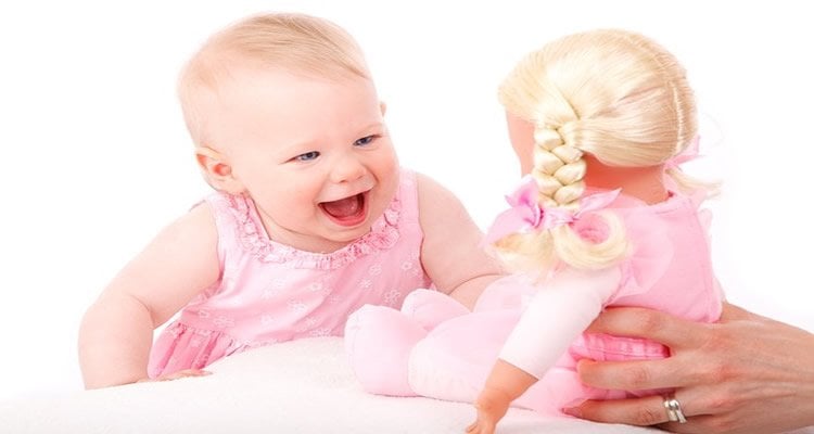 The image shows a baby girl laughing at a toy doll.