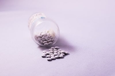 This image shows a tipped over pill jar with white pills pouring out. 