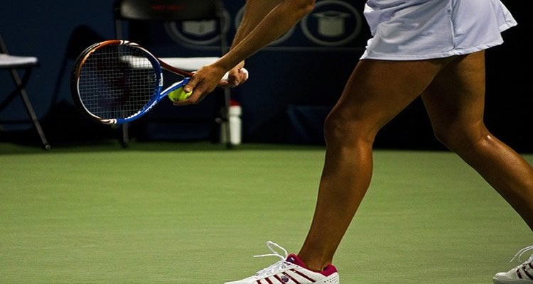 The image shows a female tennis player about to serve a ball.