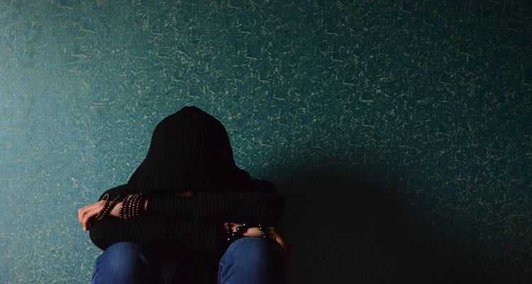 This image shows a girl sitting in the dark against a wall.