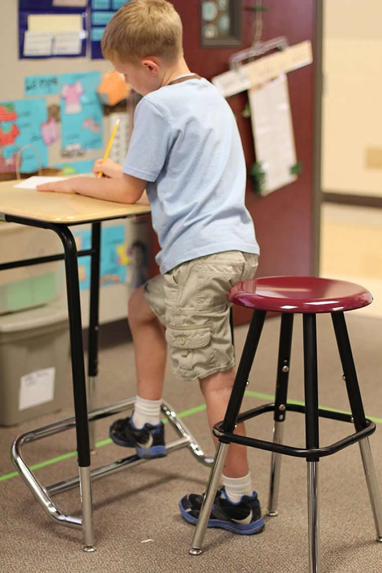 This image shows a little boy standing up at his desk.
