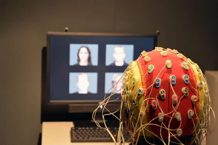 This image shows a person with a EEG cap on, looking at a computer monitor with faces on it.