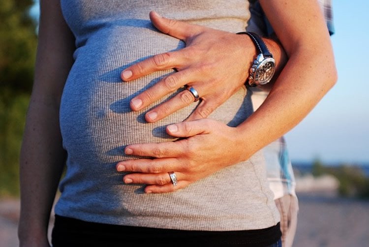 Image shows a pregnant woman with a man's hand around her belly.