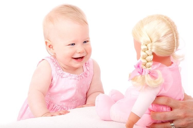 Image shows a baby looking at a doll.