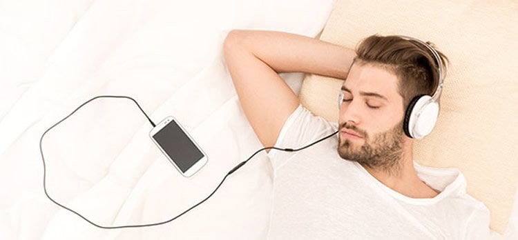 Photo of a man taking a nap while listening to his cell phone via a head set.