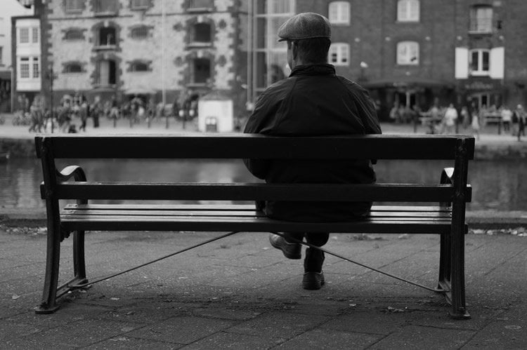 Image shows an old man sitting on a bench.
