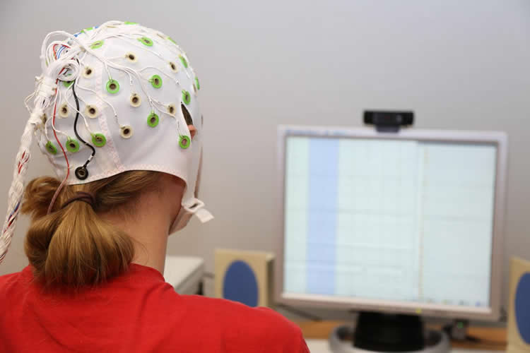 Photo of a woman in a EEG cap looking at a computer monitor.