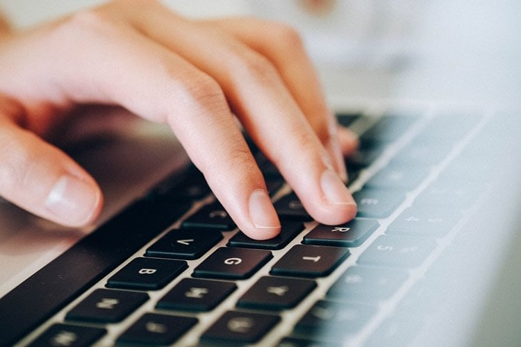 Image shows a person typing on a computer.