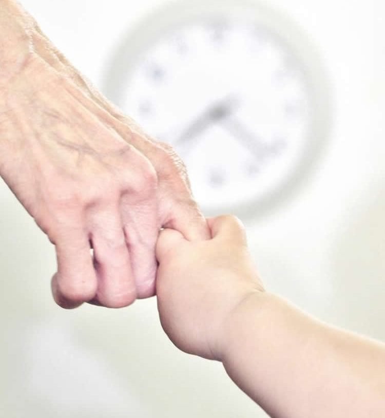 Image shows a young person holding an old person's hand.