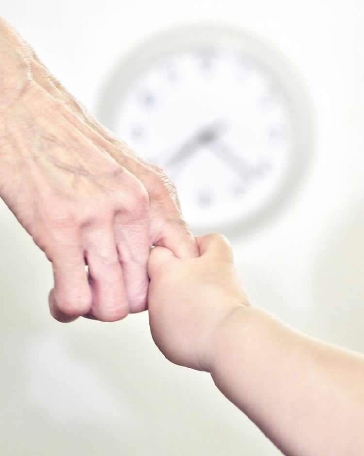 Image shows a young person holding an old person's hand.