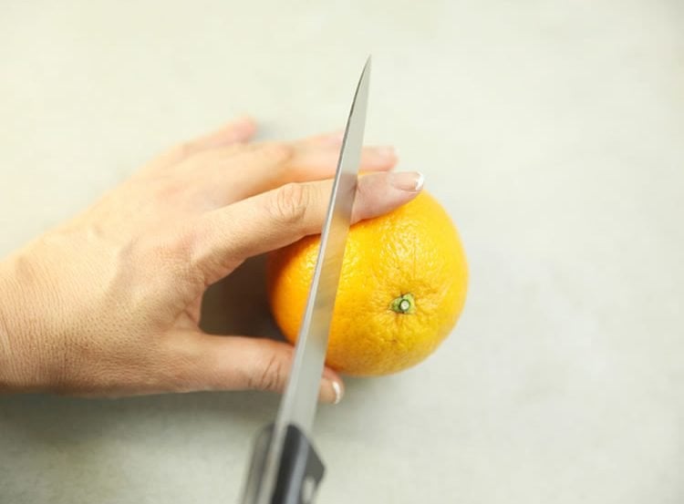 Image shows someone about to cut their finger with a knife while slicing an orange.