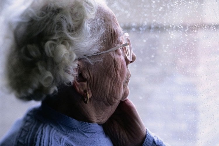 Image shows an old lady looking out of a window.