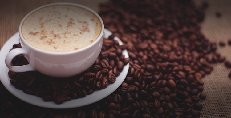 Image shows a cup of coffee and coffee beans.