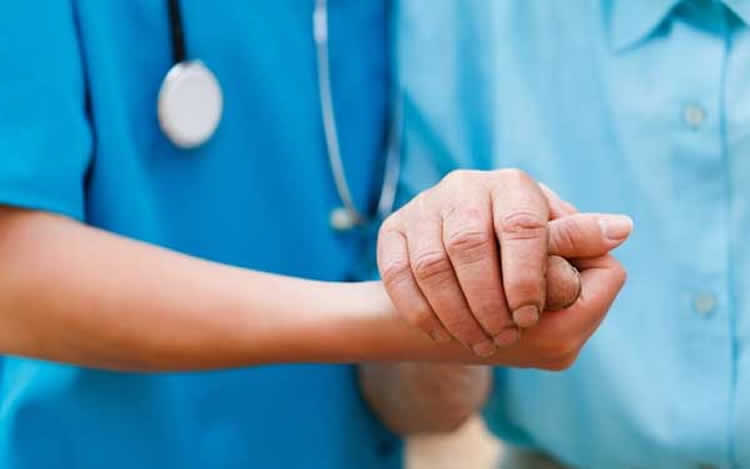 Image shows a nurse holding a person's hand.