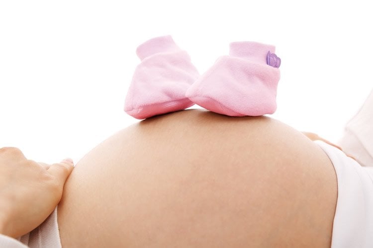 Image shows a pregant woman and baby shoes.