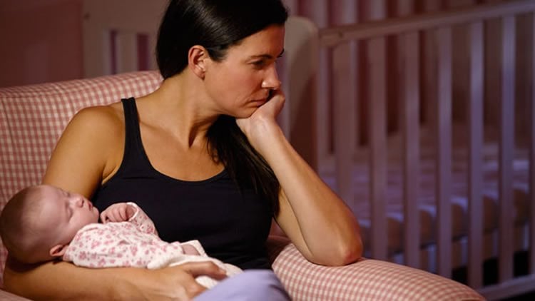 Image shows a depressed looking woman holding a baby.