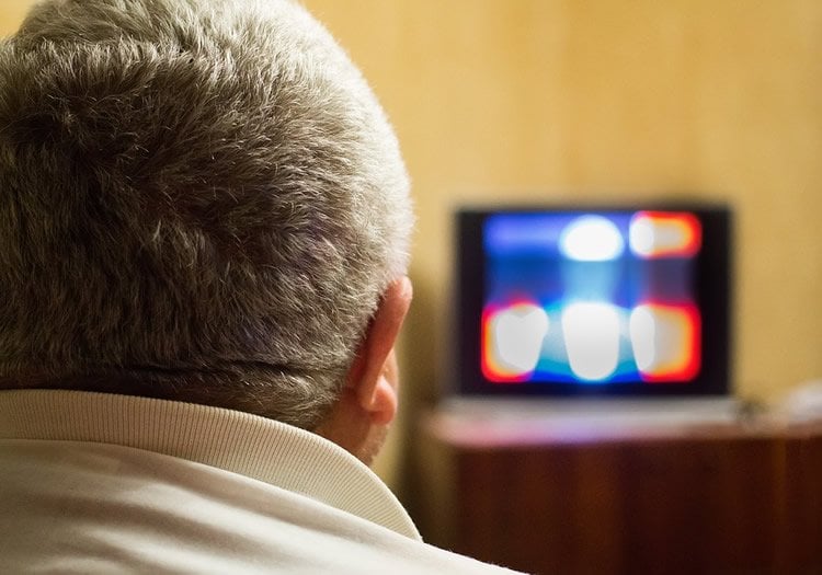 Image shows a man watching tv.