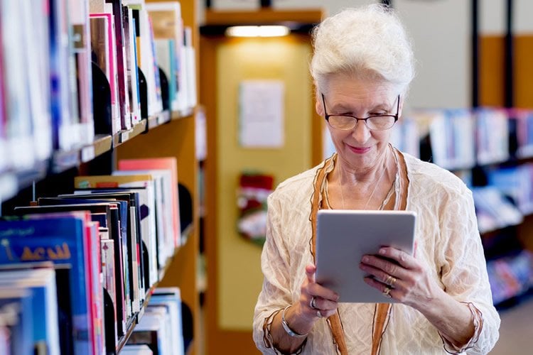 Image shows an older lady reading from a tablet.