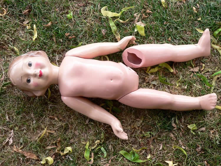 Image shows a baby doll with her leg broken off.