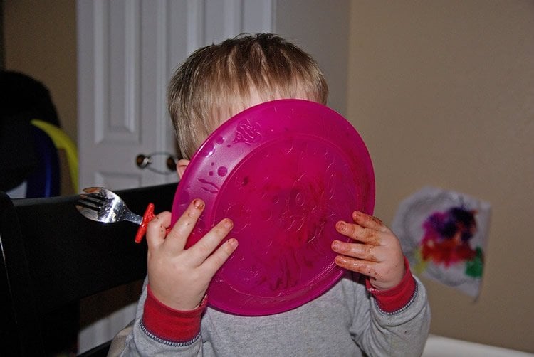 Image shows a baby licking a plate.