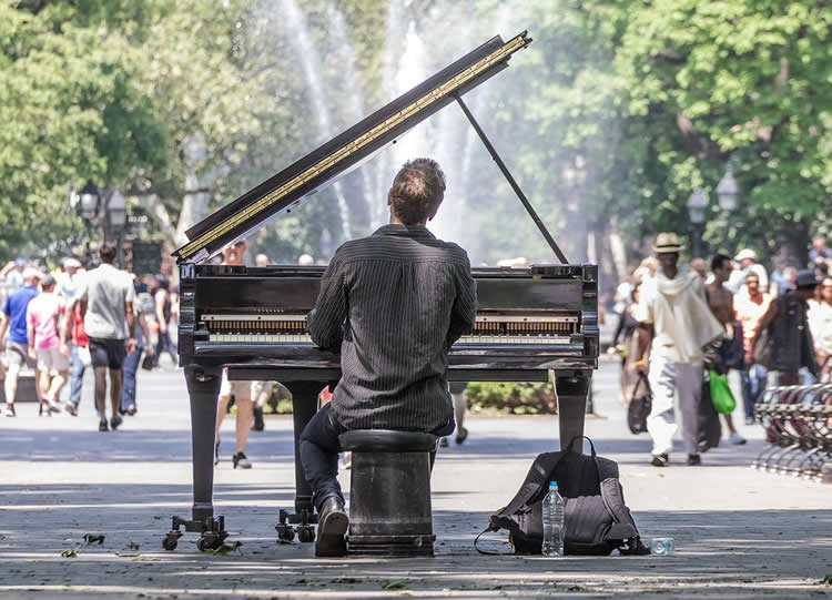 Image shows a man playing piano in a park.