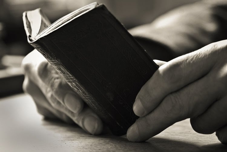 Image shows a book and a pair of old hands.