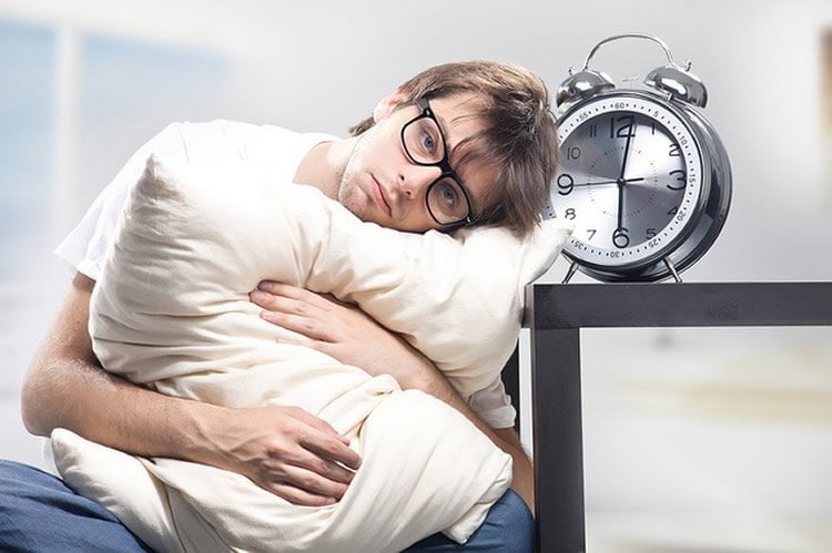 Image shows a man sitting awake with an alarm clock.