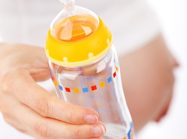 Image shows a pregnant woman holding a baby bottle.