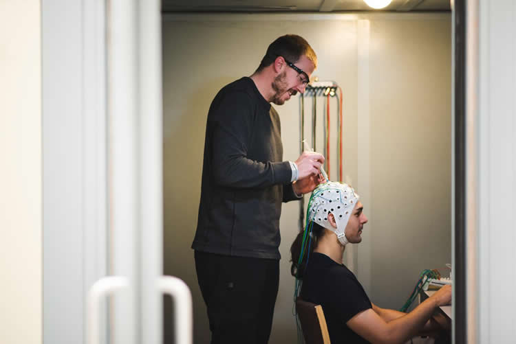 Image shows the researcher fitting an EEG cap onto a test subject.