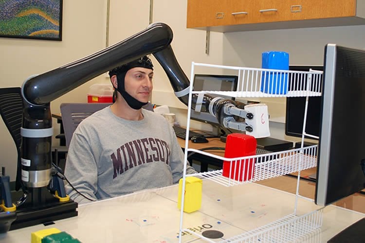 Image shows a person using the brain cap to move a robotic arm.