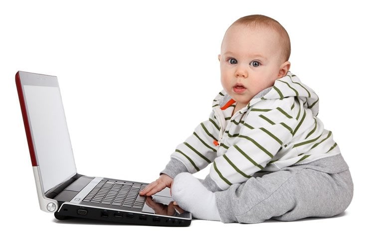 Image shows a baby playing on a laptop.