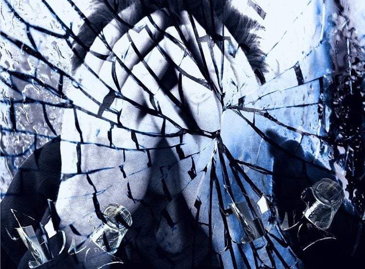 Image shows a cracked glass and a man looking as though he is in despair.