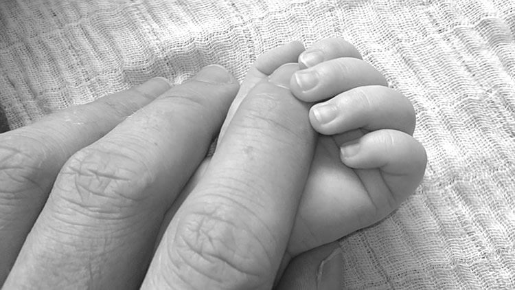 Image shows a dad holding a baby's hand.