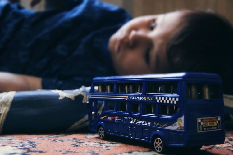 Image shows a child playing alone with a bus.