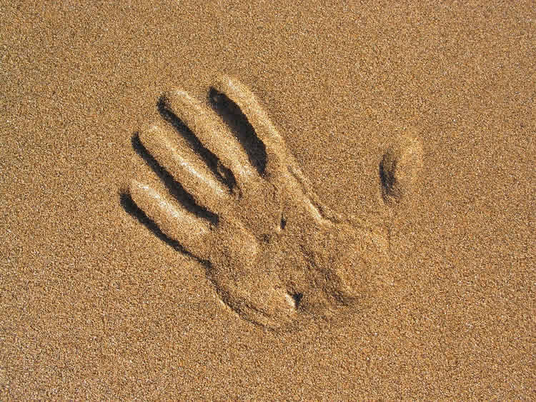 Image shows a hand print in sand.